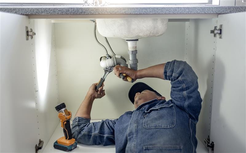 Plumber repairing pipes beneath a bathroom sink in Hawthorne